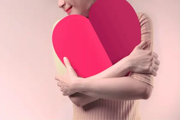 Bild für Mehr Selbstliebe leben. Zu sehen ist eine Frau, die ein Herz umarmt.